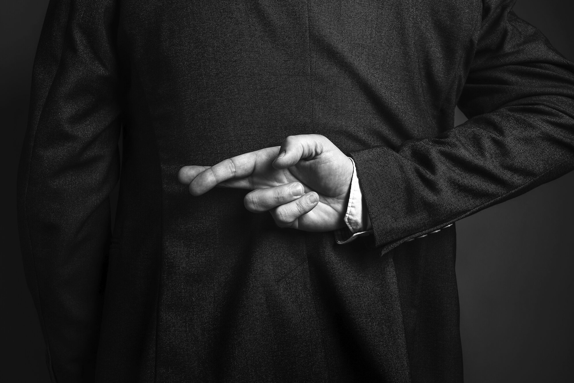 Fachsymposium Betrug - die Rückseite eines Mannes im Anzug, der hinter seinem Rücken die Finger kreuzt